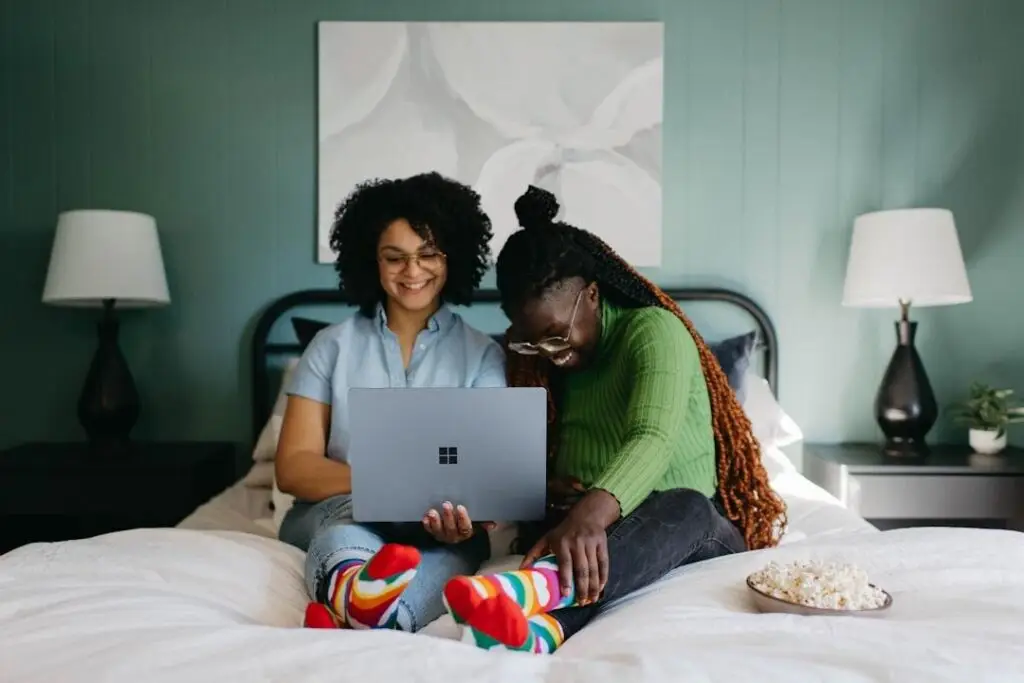 Two women smiling and sharing a Microsoft Surface laptop in a cosy home setting
