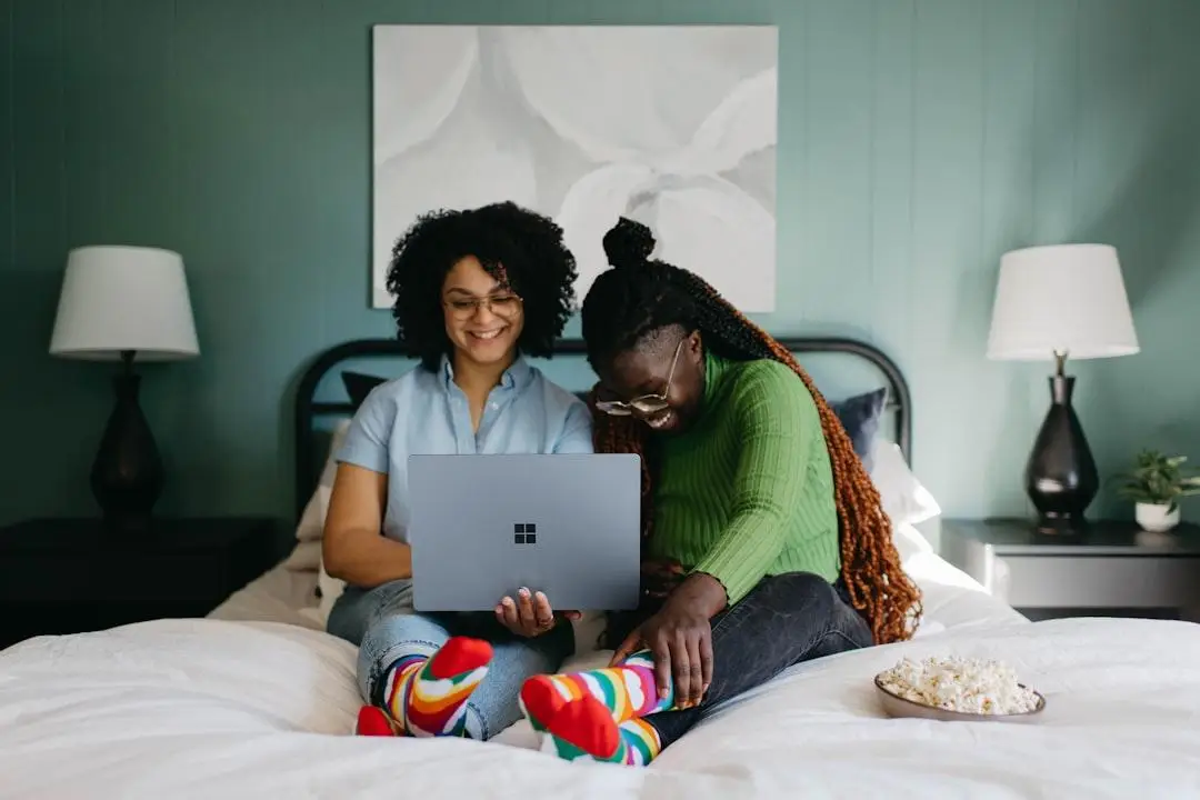 Two women smiling and sharing a Microsoft Surface laptop in a cosy home setting